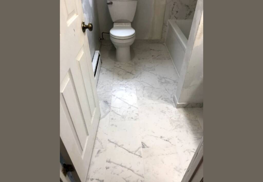 Freshly tiled bathroom floor with white marble-look tiles, installed around a toilet and bathtub example of bathroom floor tile installation cost and quality finish.