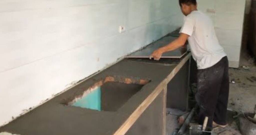Worker installing kitchen tiles on a concrete countertop, illustrating labor involved in determining kitchen tile installation cost.