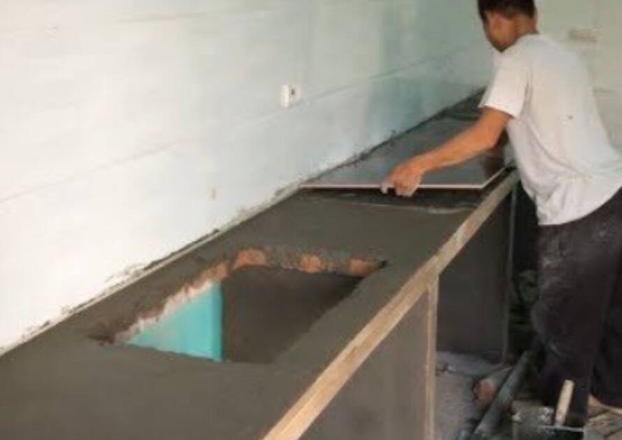 Worker installing kitchen tiles on a concrete countertop, illustrating labor involved in determining kitchen tile installation cost.