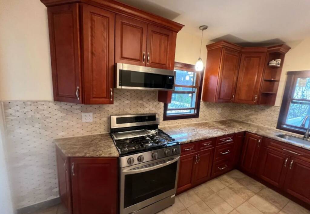 Completed kitchen wall tile installation with mosaic backsplash, granite countertops, and cherry wood cabinets – example of professional kitchen wall tile installation cost project.