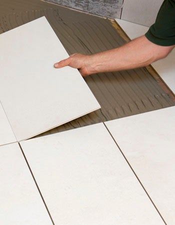 A person installing large white floor tiles over thin-set mortar, illustrating the tile installation process and considerations for tile installation cost.